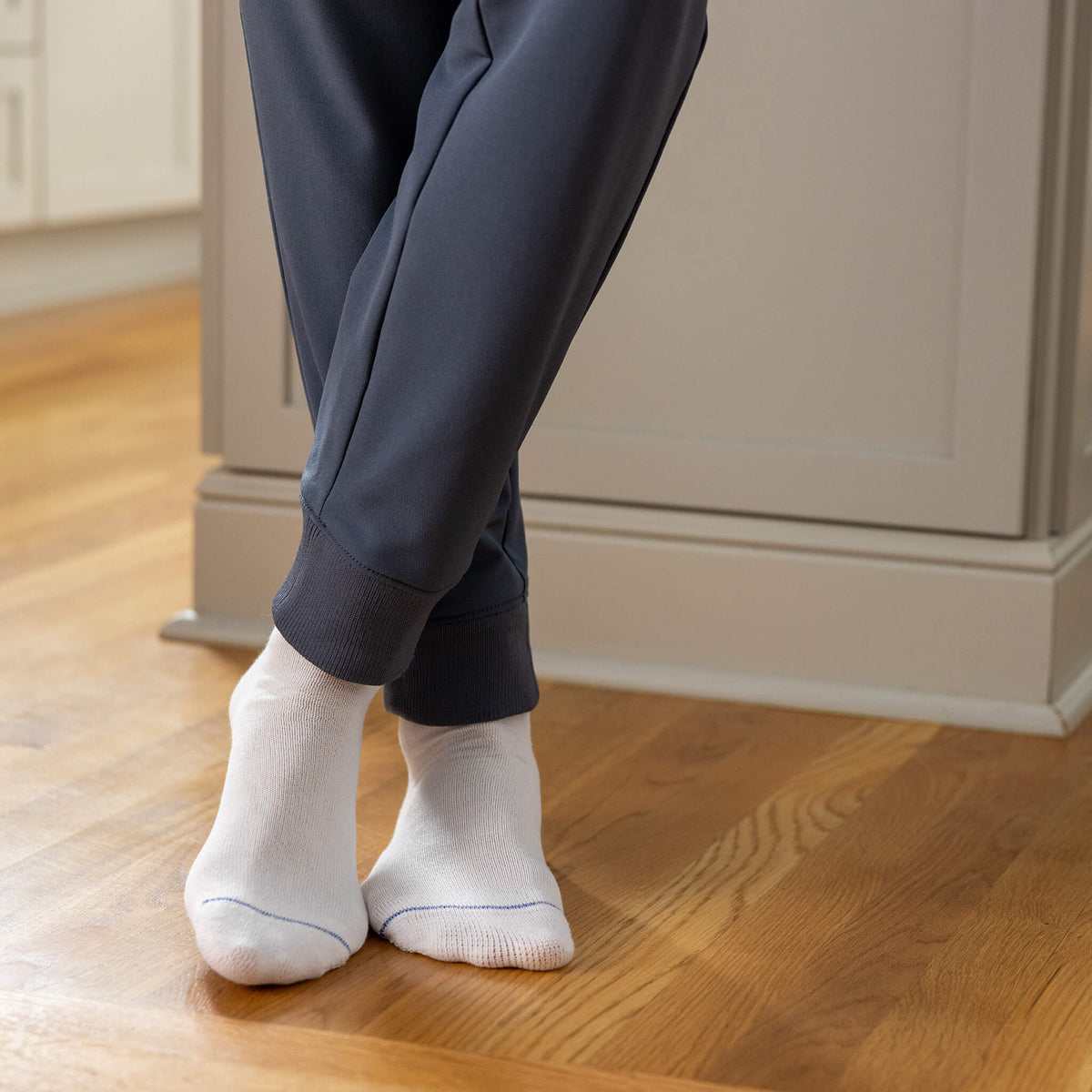 Person wearing dark pants and white socks on a wooden floor.