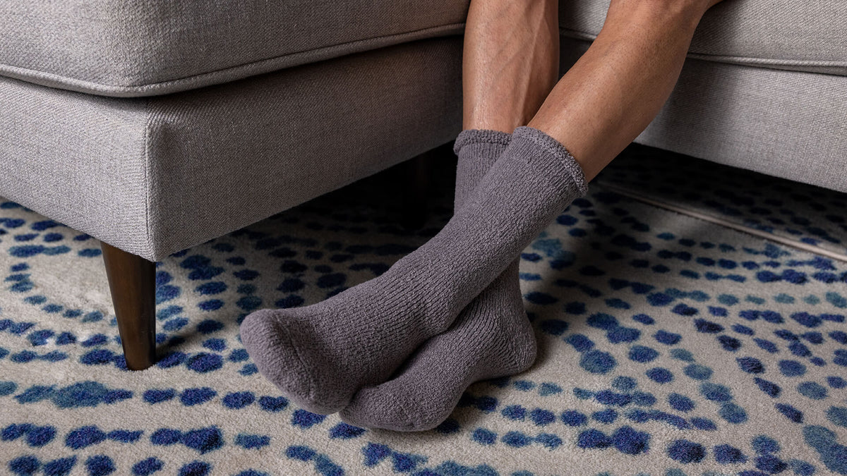 Person wearing gray socks sitting on a gray couch with a patterned rug.